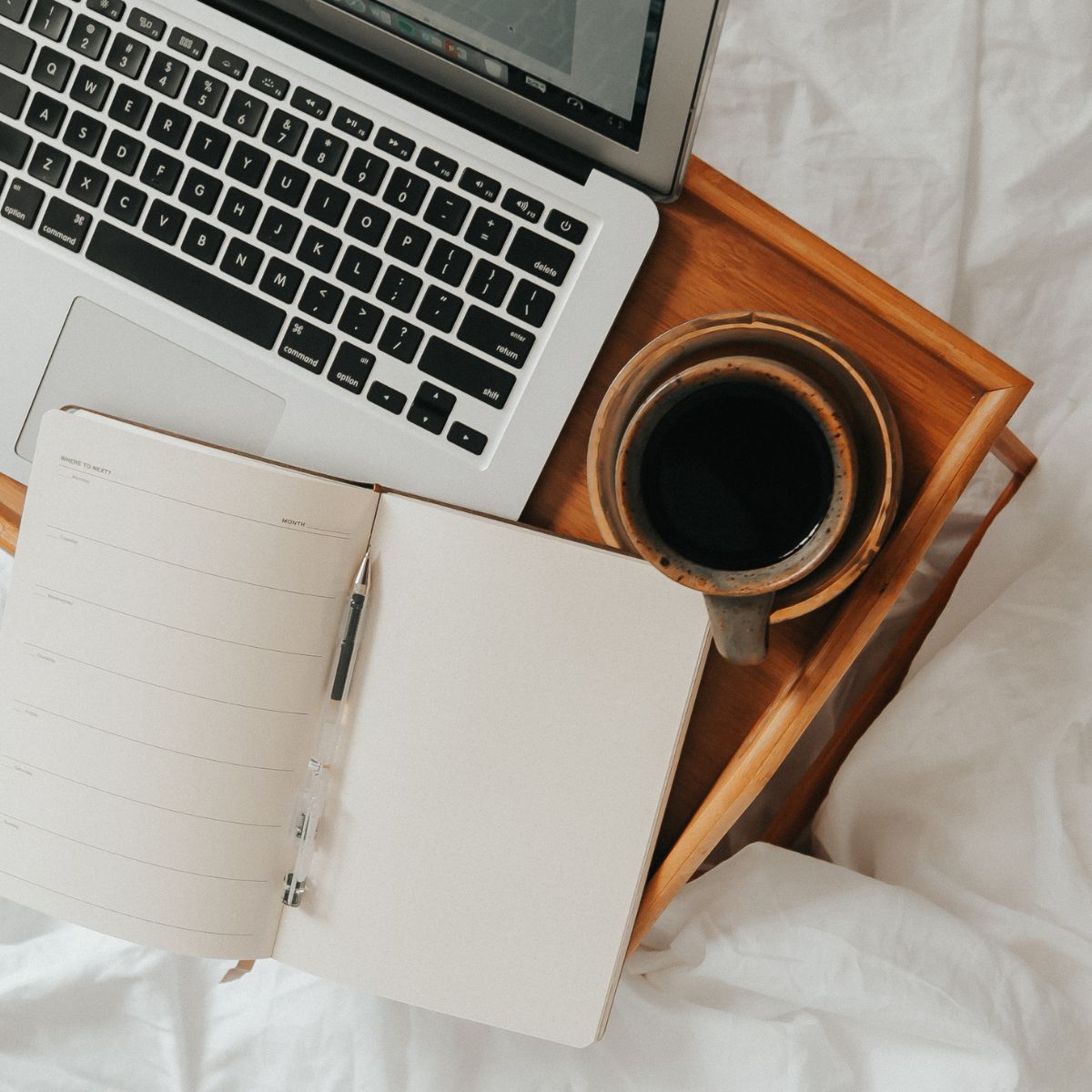 Open planner, laptop, and coffee cup on a wooden tray symbolizing planning and preparation for the egg freezing journey.