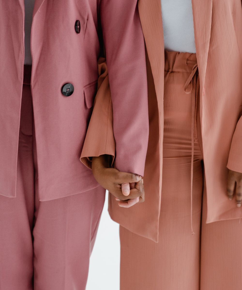 Close-up of two women holding hands, wearing pink suits, representing unity and support, by Fyrce Care