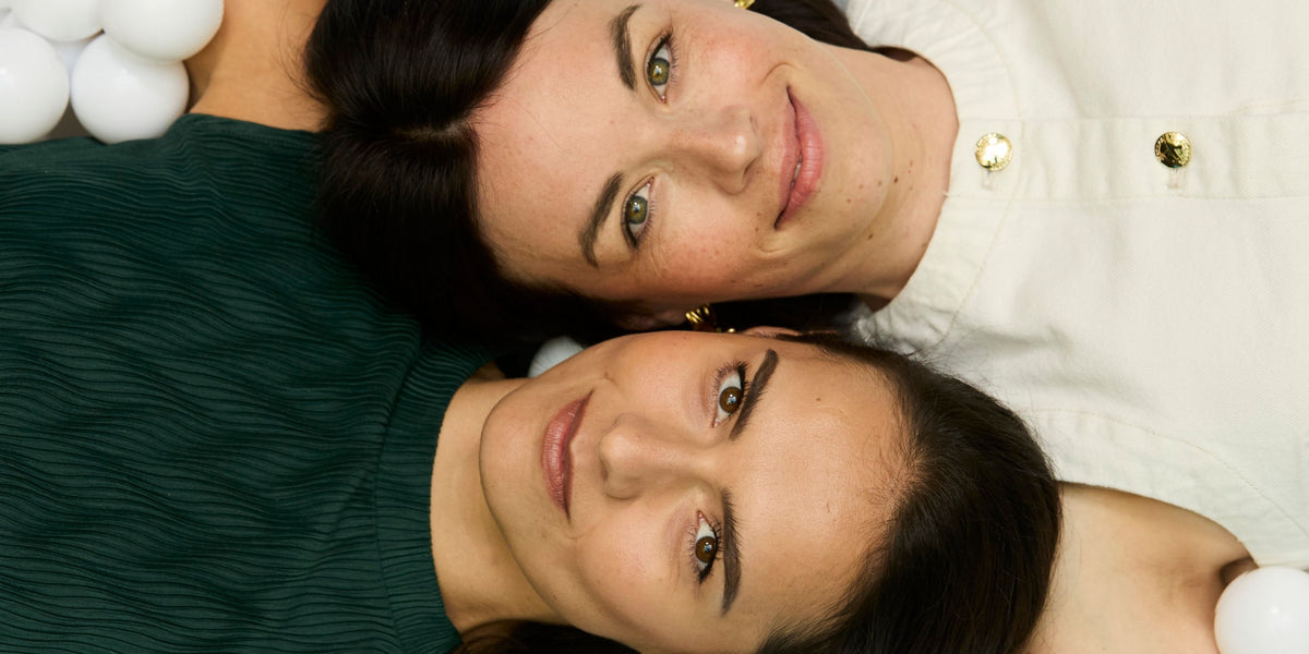 Die Fyrce Care Gründerinnen Johanna und Lisa liegen Kopf an Kopf auf dem Boden und lächeln.