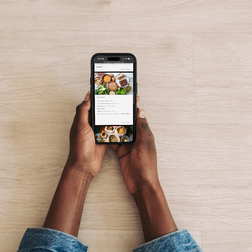 Hands holding a smartphone showing a recipe in the Fyrce Grow app, with plant-based ingredients like legumes, nuts and greens